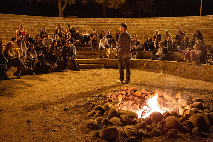 Spectators listen to a man tell a story by a fire. Storytelling in content marketing increases engagement with audiences.